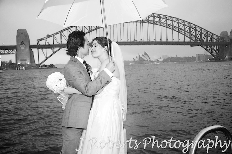 Bride and groom kissing under an umbrella with Sydney Harbour in the background - wedding photography sydney